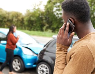 Man on the phone at the scene of an auto accident.